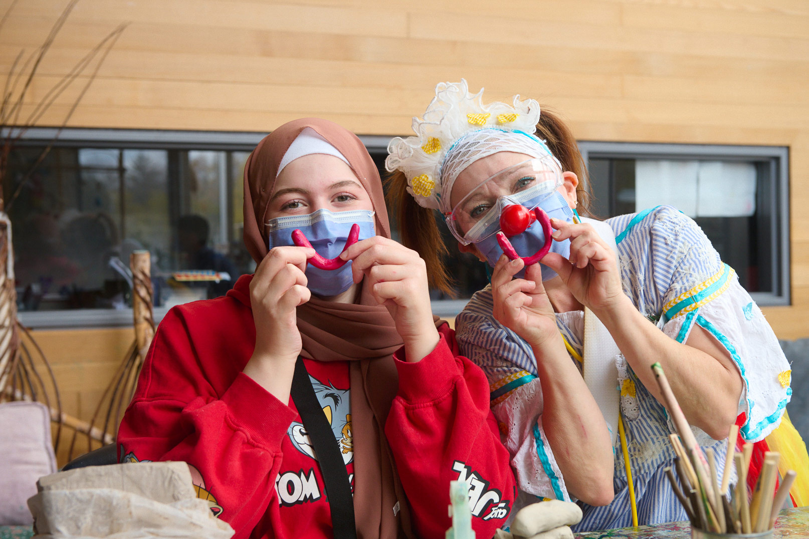 A young person and a therapeutic clown hold clay smile-shaped figurines