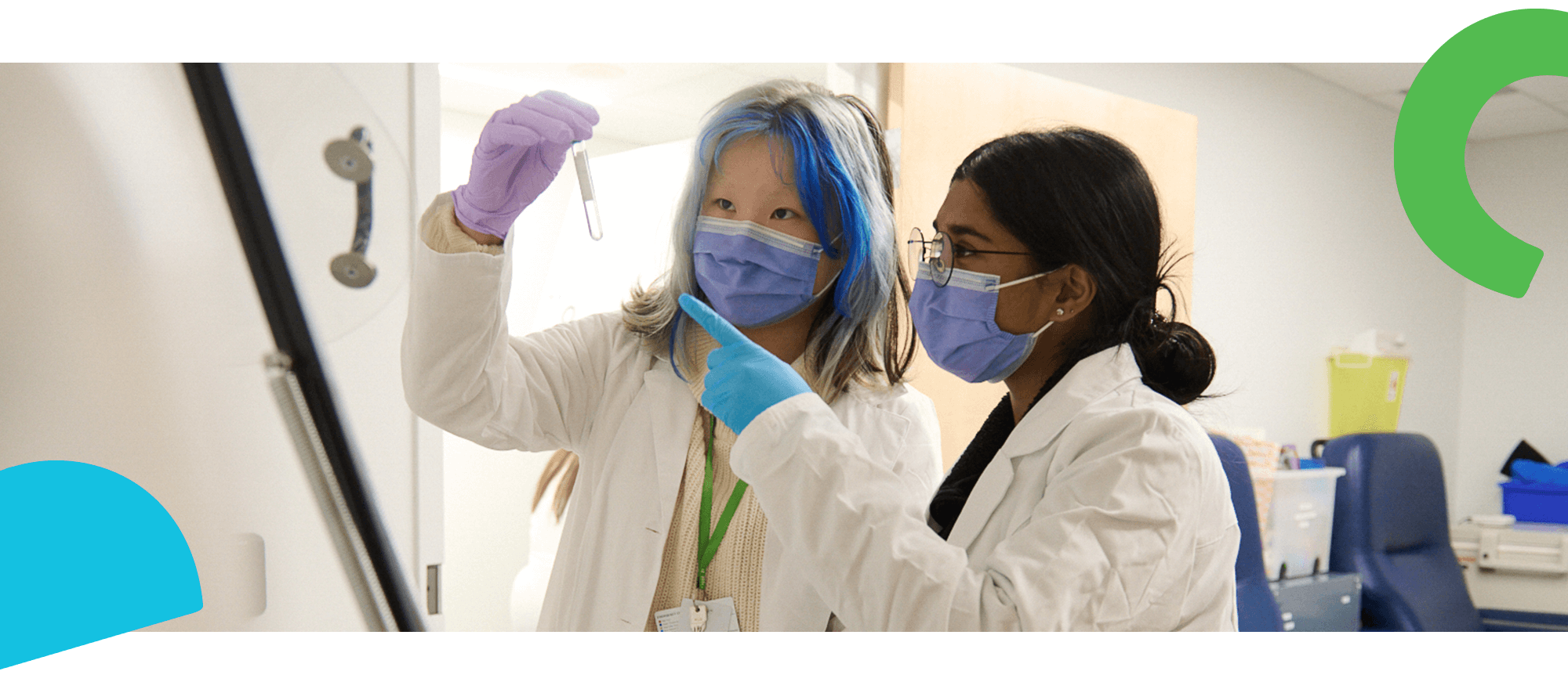 Two scientists wear face masks and observe a test tube