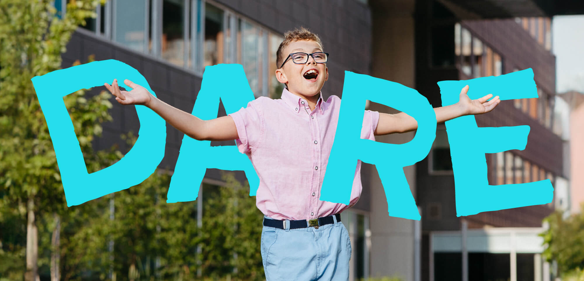 A young boy joyfully spreading his arms outdoors in front of Holland Bloorview