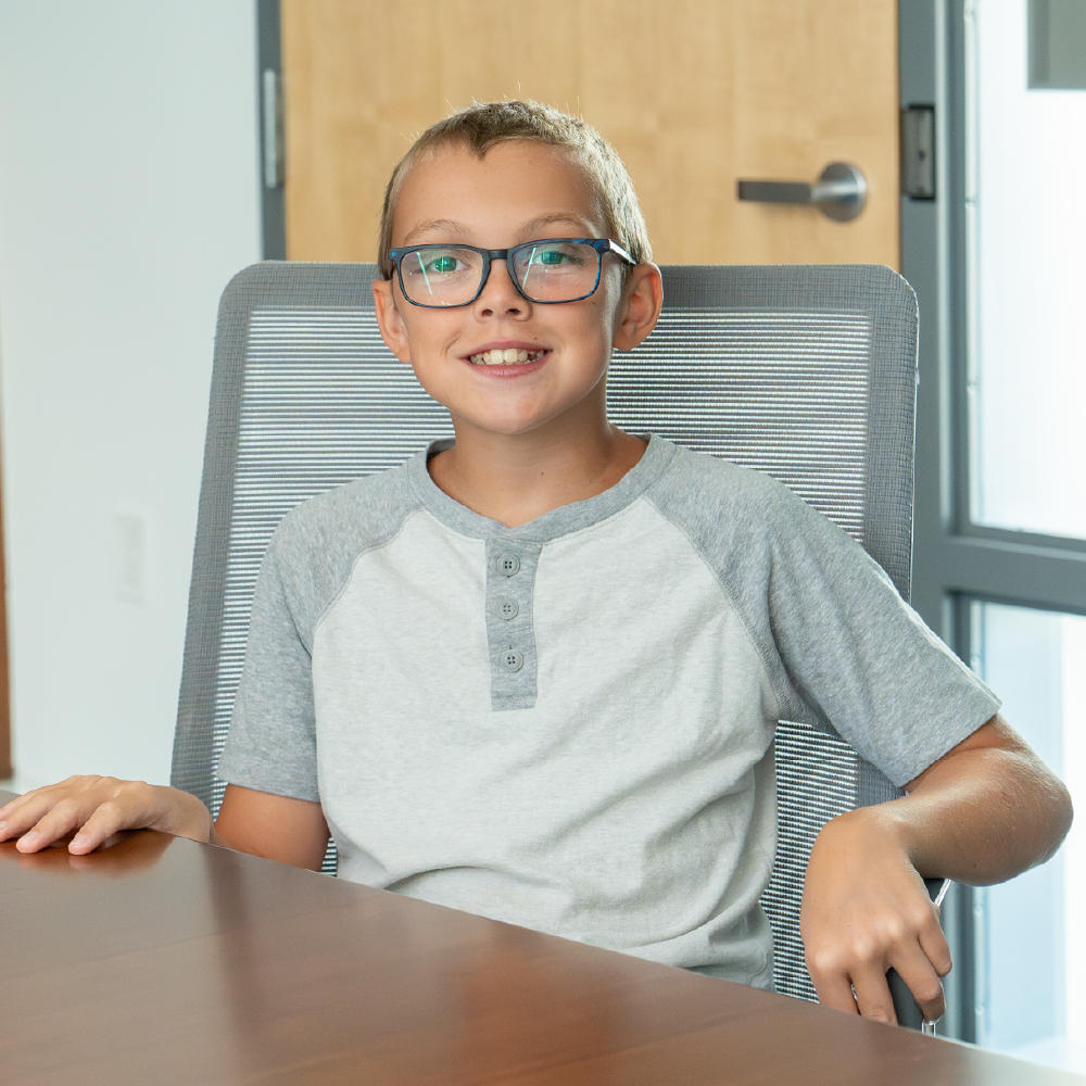 A young boy smiles while sitting in a board room