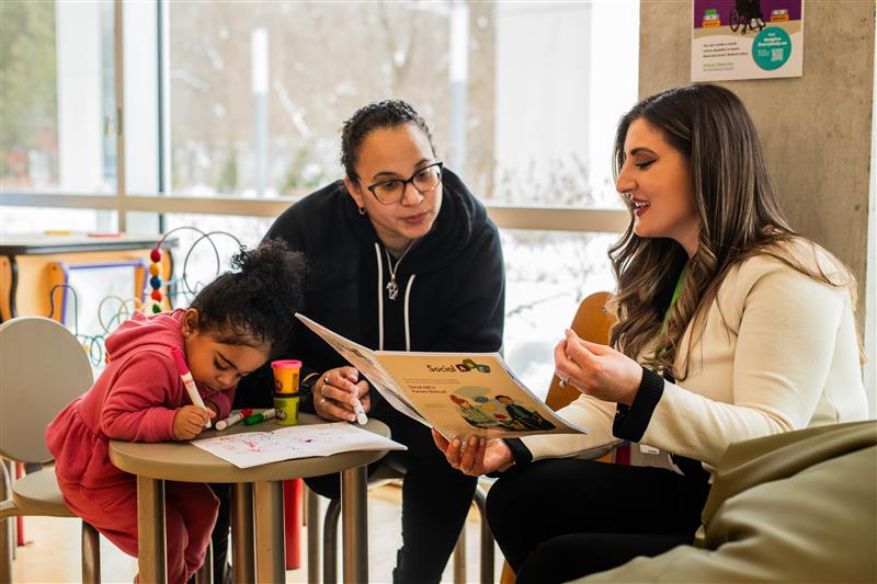 Two adults and a child read and colour