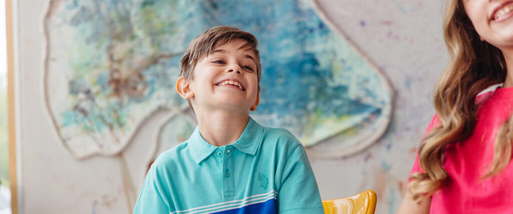 A young boy smiles in front of a large colourful painting