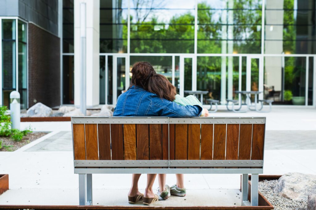 A mother and her child embrace while sitting on an outdoor bench