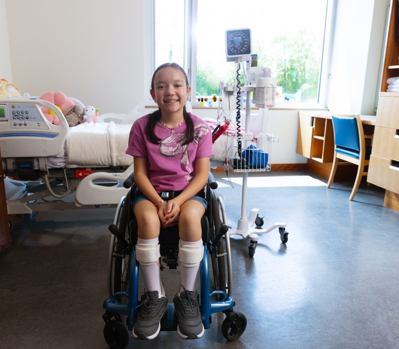 A young girl who uses a wheelchair smiles and sits in an inpatient hospital room