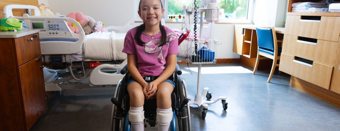 A young girl who uses a wheelchair smiles and sits in an inpatient hospital room
