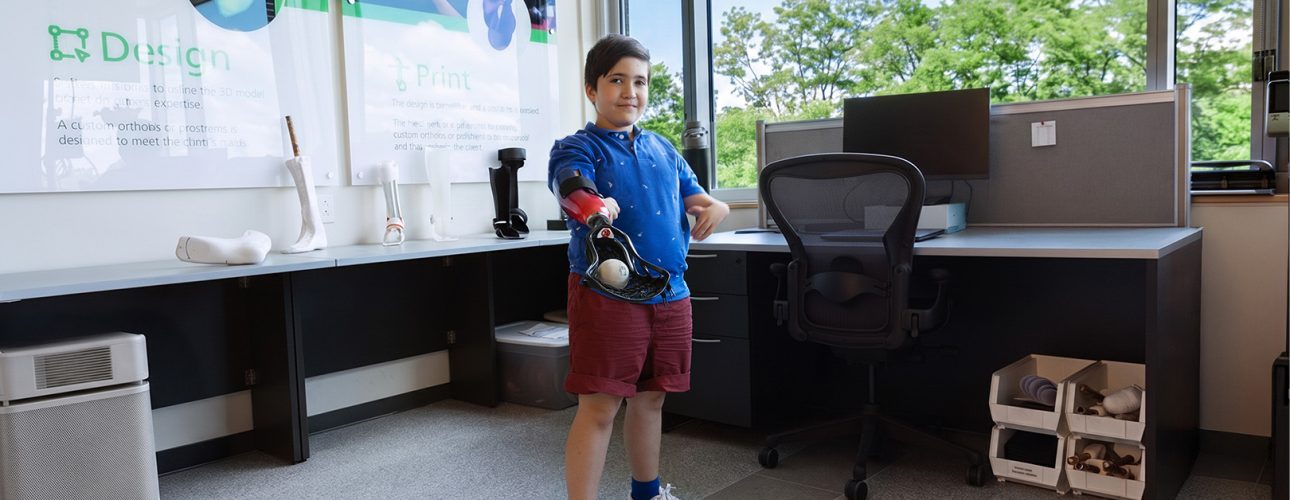 A young boy plays with a ball using his lacrosse prosthetic
