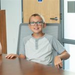 Alex A young boy smiles while sitting in a board room