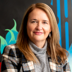 Catherine Roche An adult wears a checkered suit in front of a colourful background