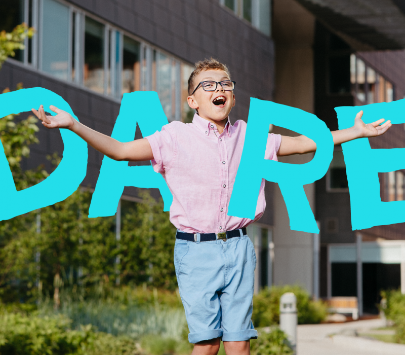 A young boy joyfully spreading his arms outdoors in front of Holland Bloorview
