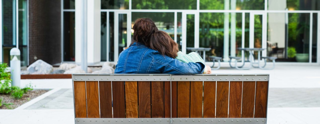 A mother and her child embrace while sitting on an outdoor bench