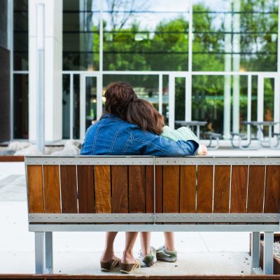 A mother and her child embrace while sitting on an outdoor bench