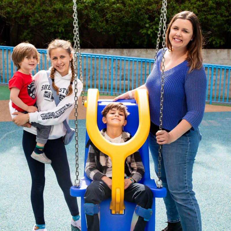 A family smiles and plays on an accessible playground swing