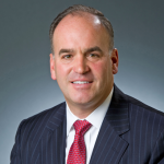 JR An adult wears a suit in front of a grey background