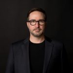 Phil Labbe An adult wears a suit in front of a black background