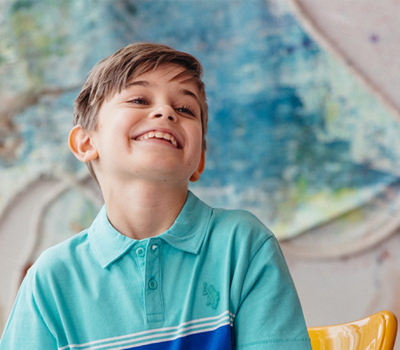 A young boy smiles in front of a large colourful painting