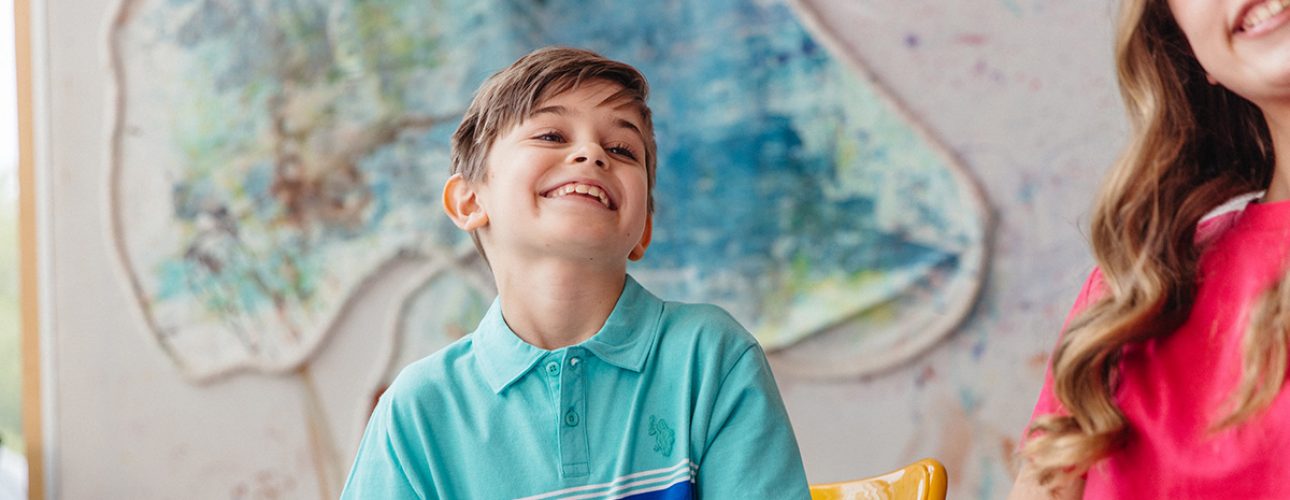 A young boy smiles in front of a large colourful painting