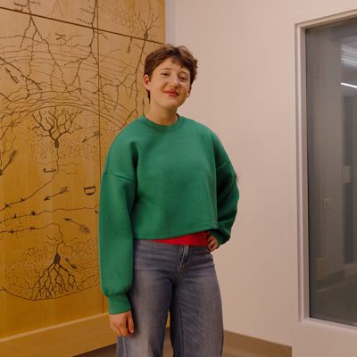 A teenager wears a bright green sweater and stands with one arm on her hip