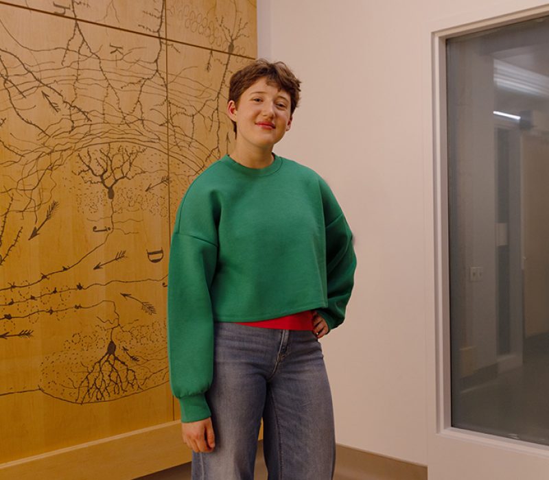 A teenager wears a bright green sweater and stands with one arm on her hip