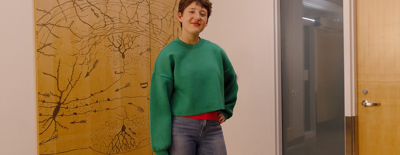 A teenager wears a bright green sweater and stands with one arm on her hip