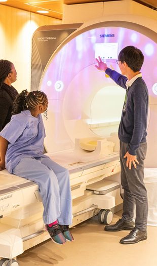 about1 A child wearing hospital clothing and two adults look at a MRI machine
