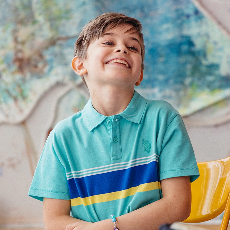 A young boy smiles and stands in front of colourful paintings