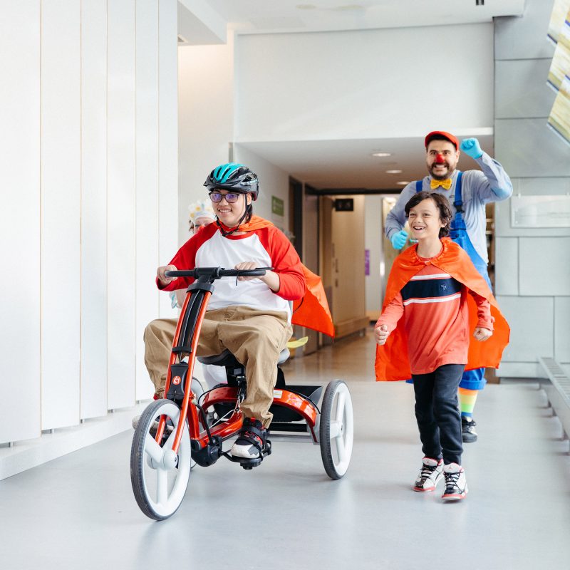 A teenager uses an adaptive bike to race another child and a therapeutic clown