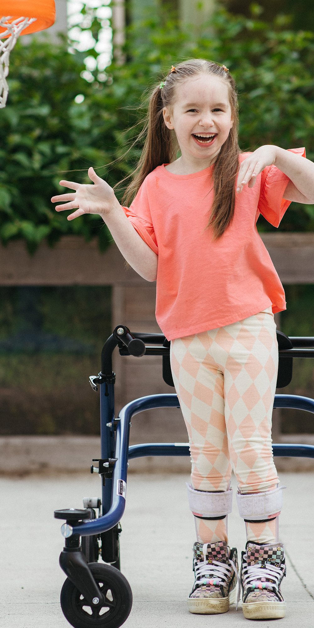 A child using a wheeled walker plays basketball outside