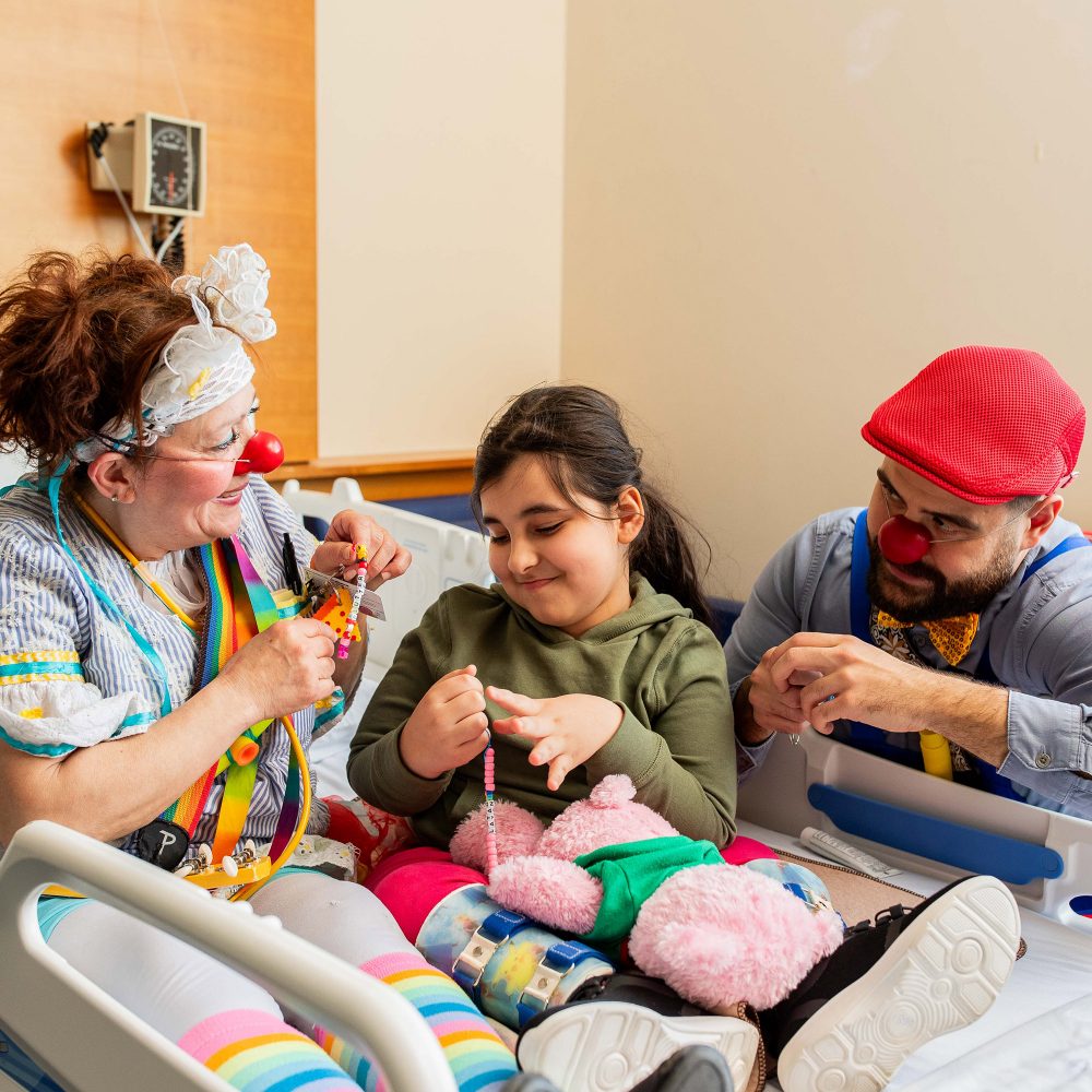 Two therapeutic clowns play with a child in a hospital bed