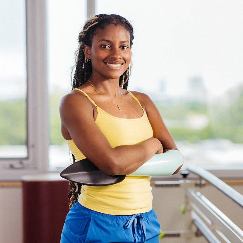 A young woman wears a prosthetic arm and poses with her arms crossed